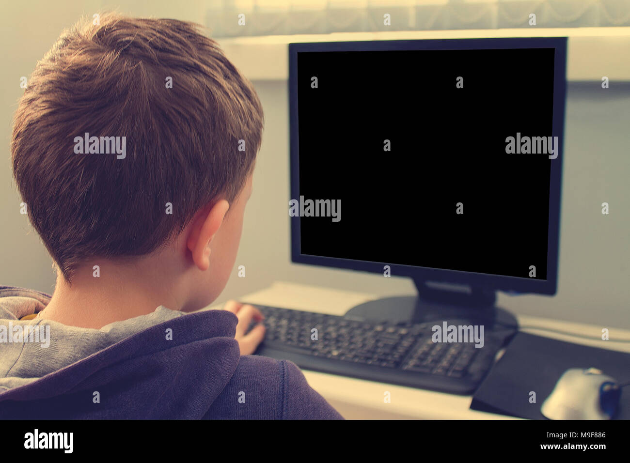 Junior schoolboy utilizzando Pc indagando il browser internet per i compiti a casa e giocare il gioco online mmorpg. La foto ha un copyspace. Foto Stock