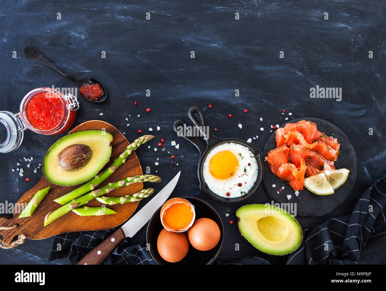 Vista superiore del tavolo per la colazione con uova fritte, avocado, asparagi, caviale rosso e salmone affumicato, spazio di copia Foto Stock