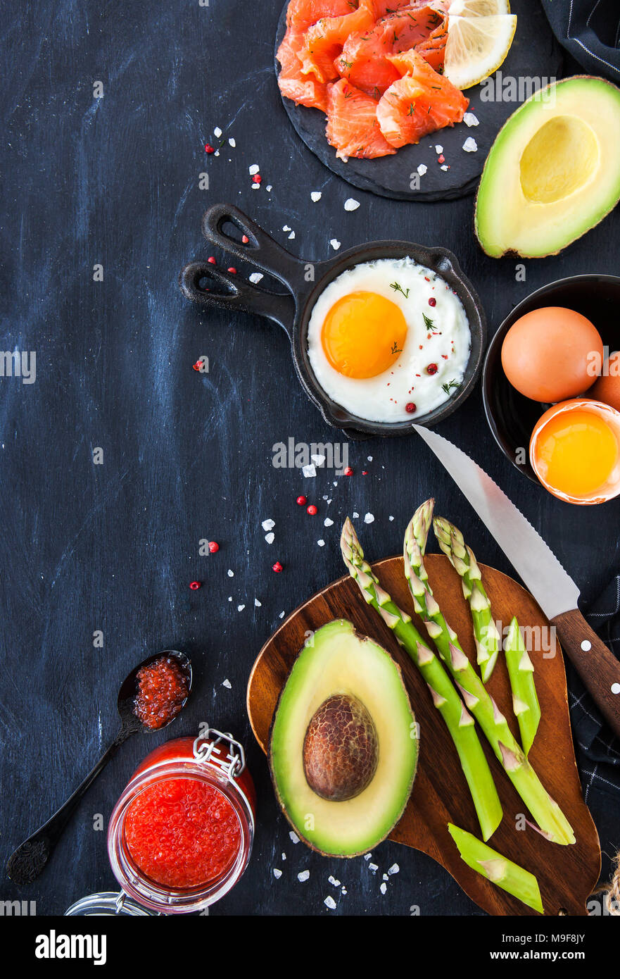 Vista superiore del tavolo per la colazione con uova fritte, avocado, asparagi, caviale rosso e salmone affumicato, spazio di copia Foto Stock