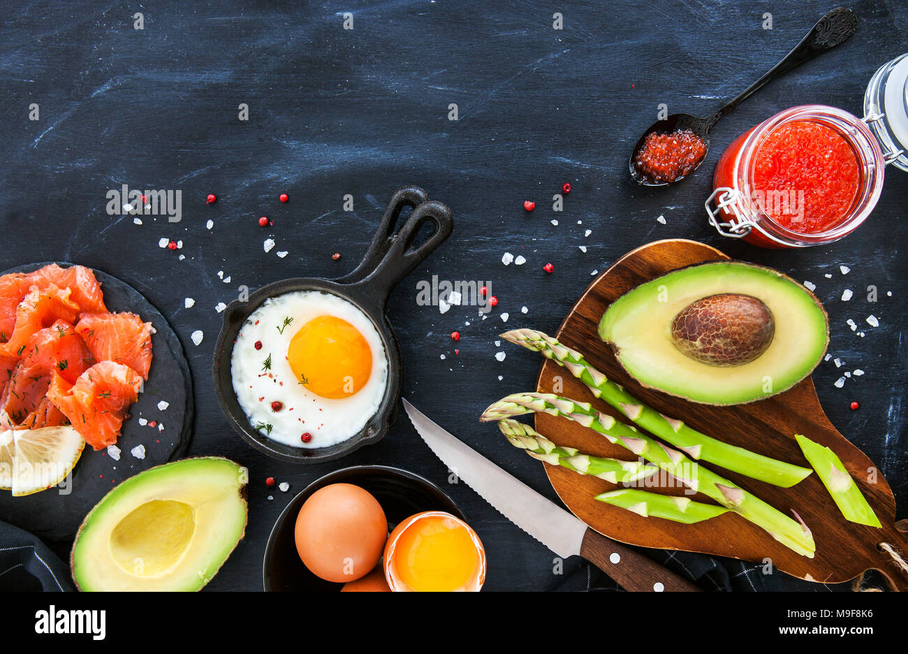 Vista superiore del tavolo per la colazione con uova fritte, avocado, asparagi, caviale rosso e salmone affumicato, spazio di copia Foto Stock