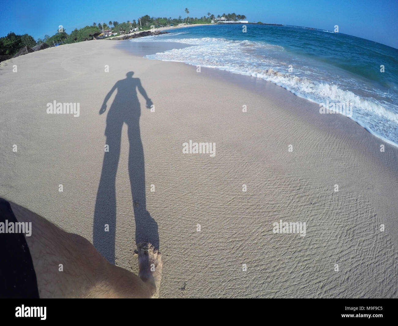 Lunga ombra di un uomo sulla spiaggia da oceano blu acqua in estate Foto Stock