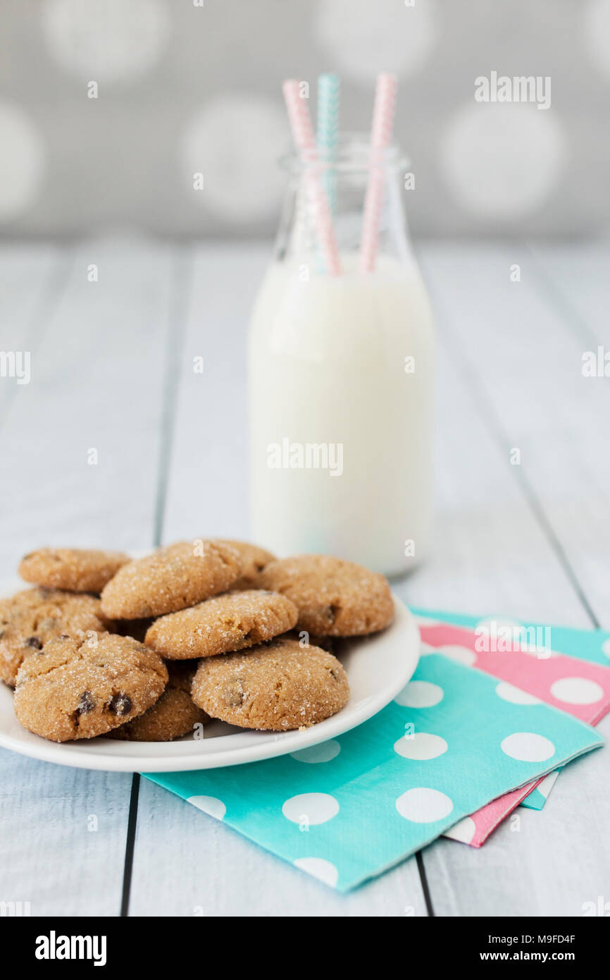 Senza glutine biscotti con scaglie di cioccolato con una bottiglia di latte su un bianco sullo sfondo di legno. Foto Stock