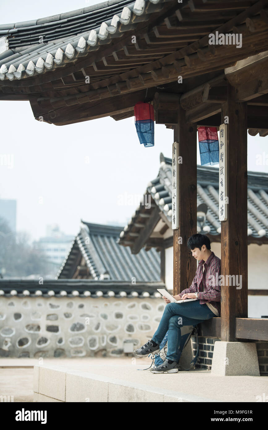 Un giovane uomo con lo zaino in spalla in Corea. utilizzando un laptop seduto in un Coreano casa tradizionale. Foto Stock