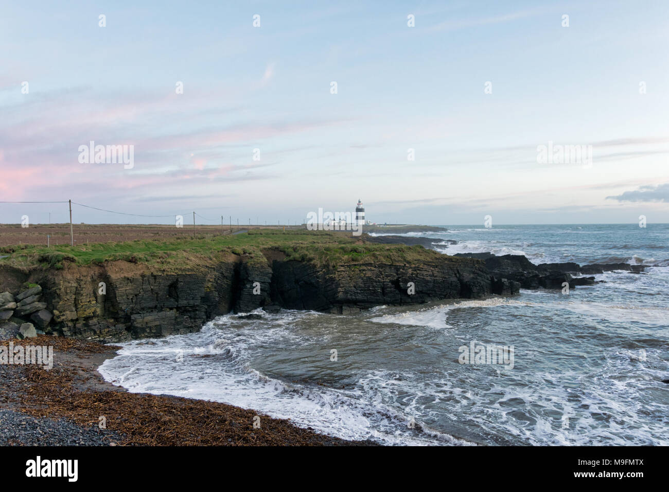 Irlandese casa di luce su una costa rocciosa con onde che si infrangono ione fino alla riva. Foto Stock