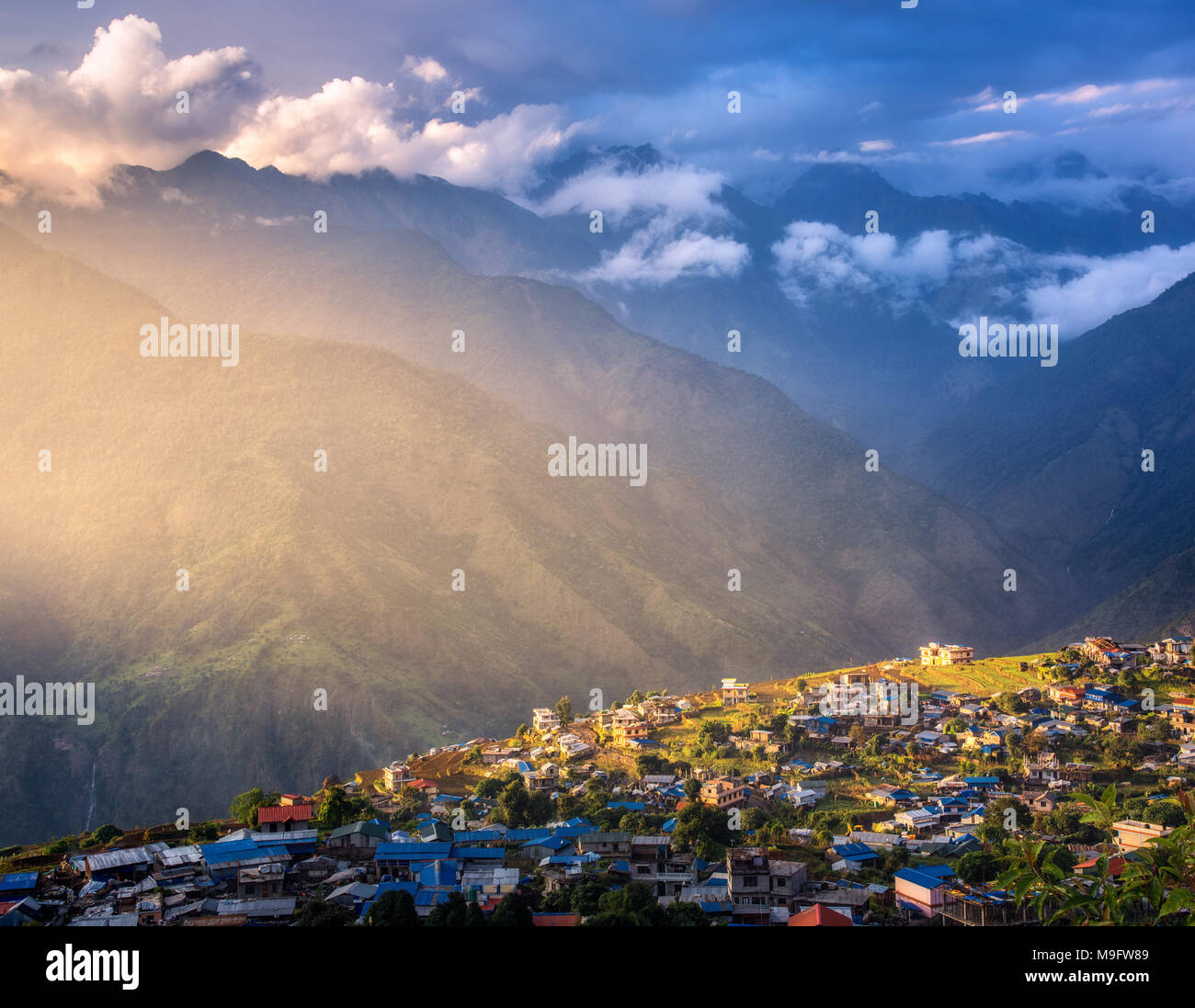 Incredibile villaggio sulla collina illuminata da un sole al tramonto in Nepal. Paesaggio con case, cielo blu con nuvole, giallo luce solare e di alta montagna w Foto Stock