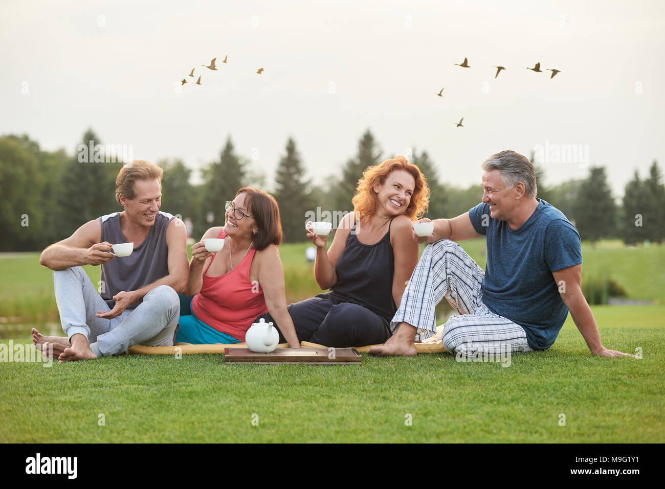 Coppie allegre seduta nel parco. Senior sorridente gli amici a bere caffè e divertirsi. Foto Stock