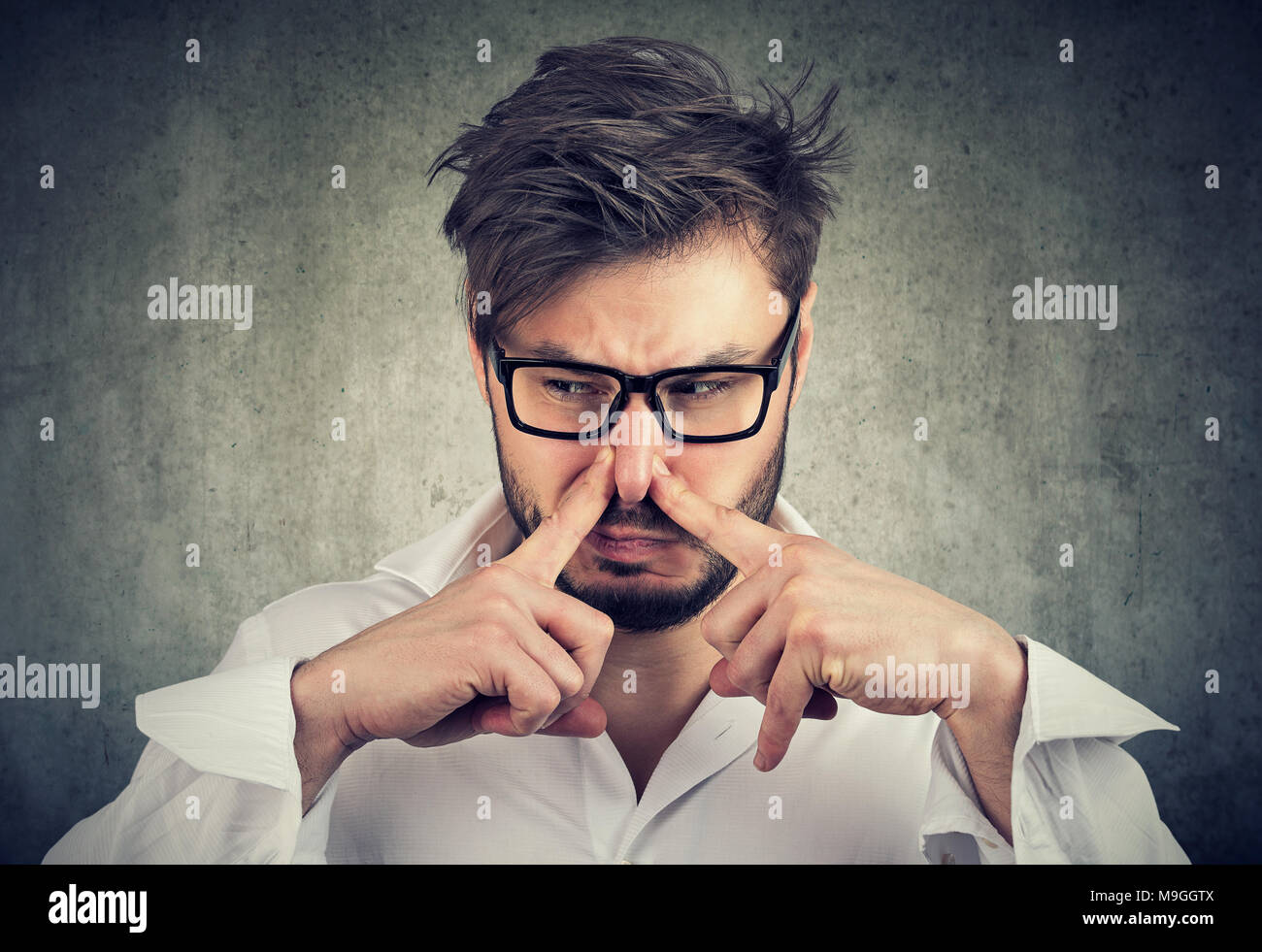 L'uomo pizzichi di naso con le dita guarda con disgusto puzza qualcosa di cattivo odore isolato su sfondo grigio. Foto Stock