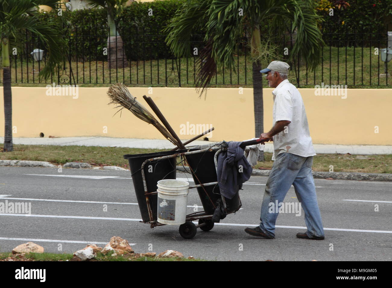 Un uomo spinge un carrello davanti a lui. Il carrello è dotato di contenitori per mettere immondizia e utensili come scopa. Foto Stock