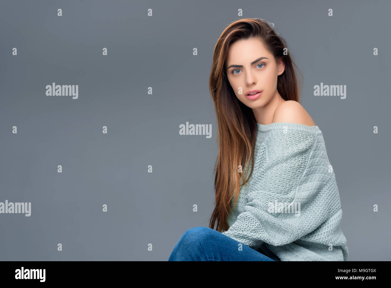 Attraente ragazza elegante in un maglione guardando la telecamera, isolato su grigio Foto Stock