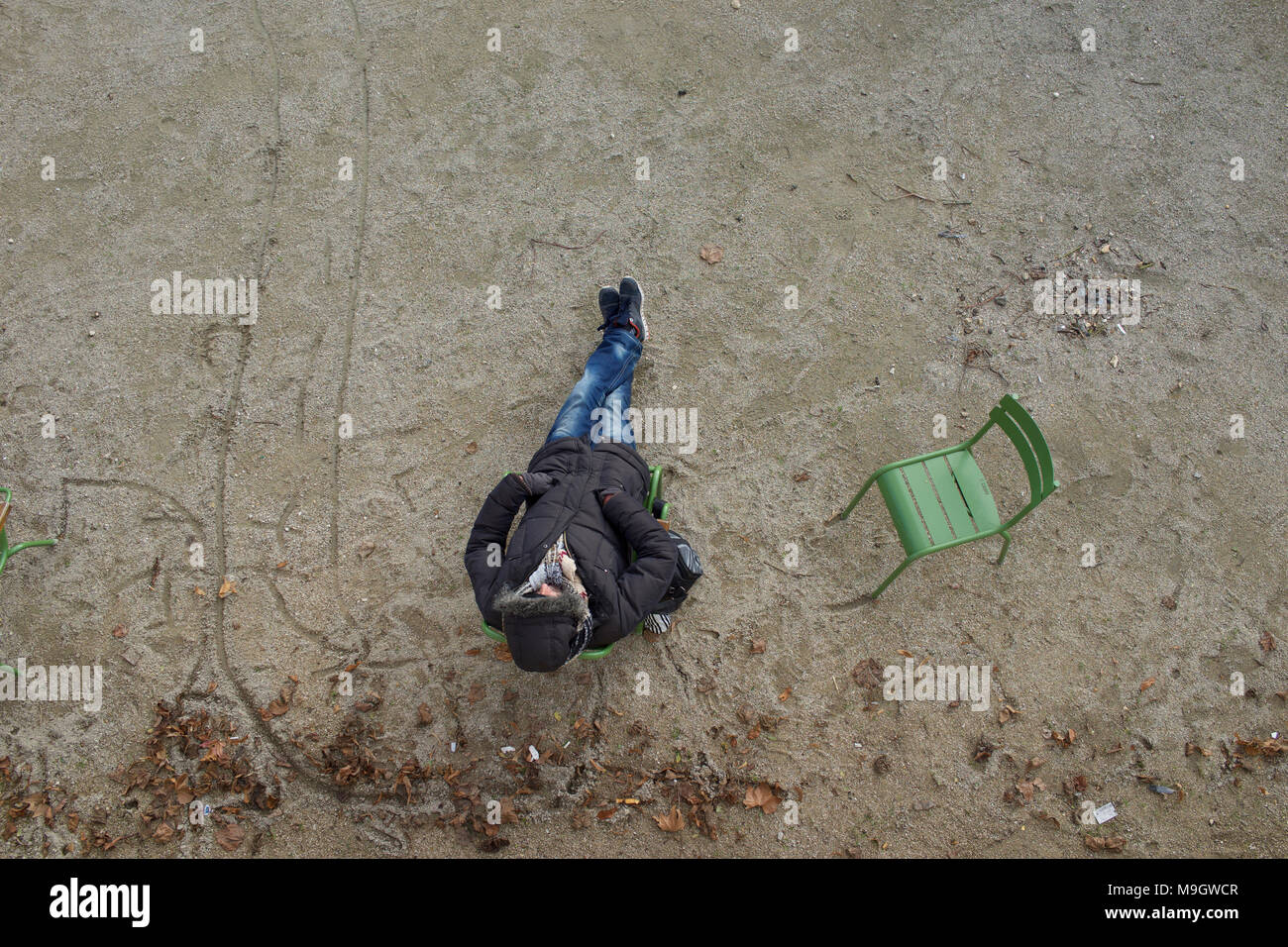 Uomo seduto su una sedia nel parco della città indossando cappotto e cappa, dormire, con le mani nelle tasche - vista aerea Foto Stock