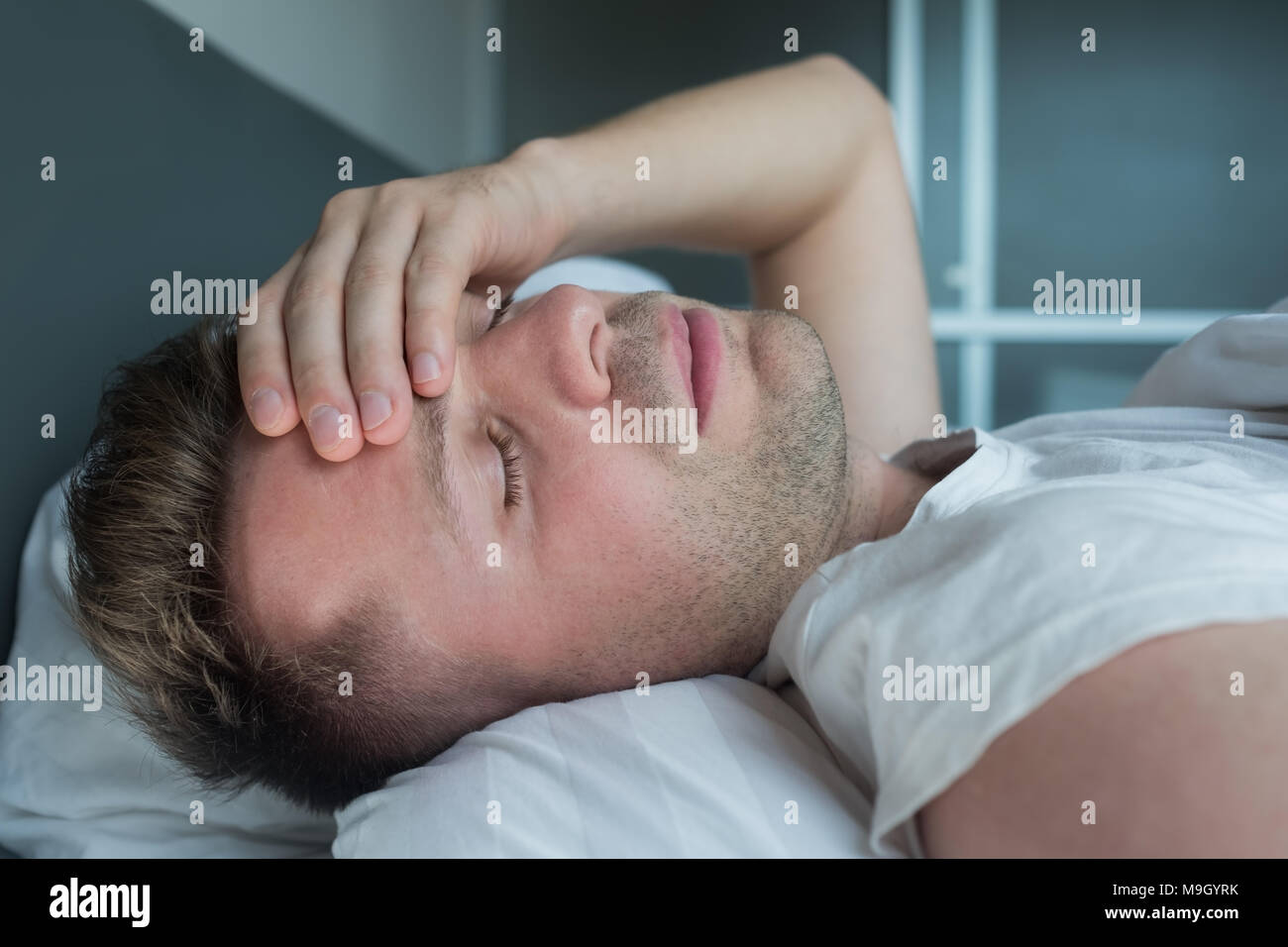 Uomo disteso nel letto di casa che soffrono di mal di testa o i postumi della sbornia Foto Stock