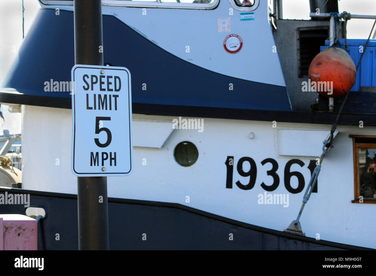 Segnale di limite di velocità sul dock al pescatore del terminale. Barca da pesca in background Foto Stock
