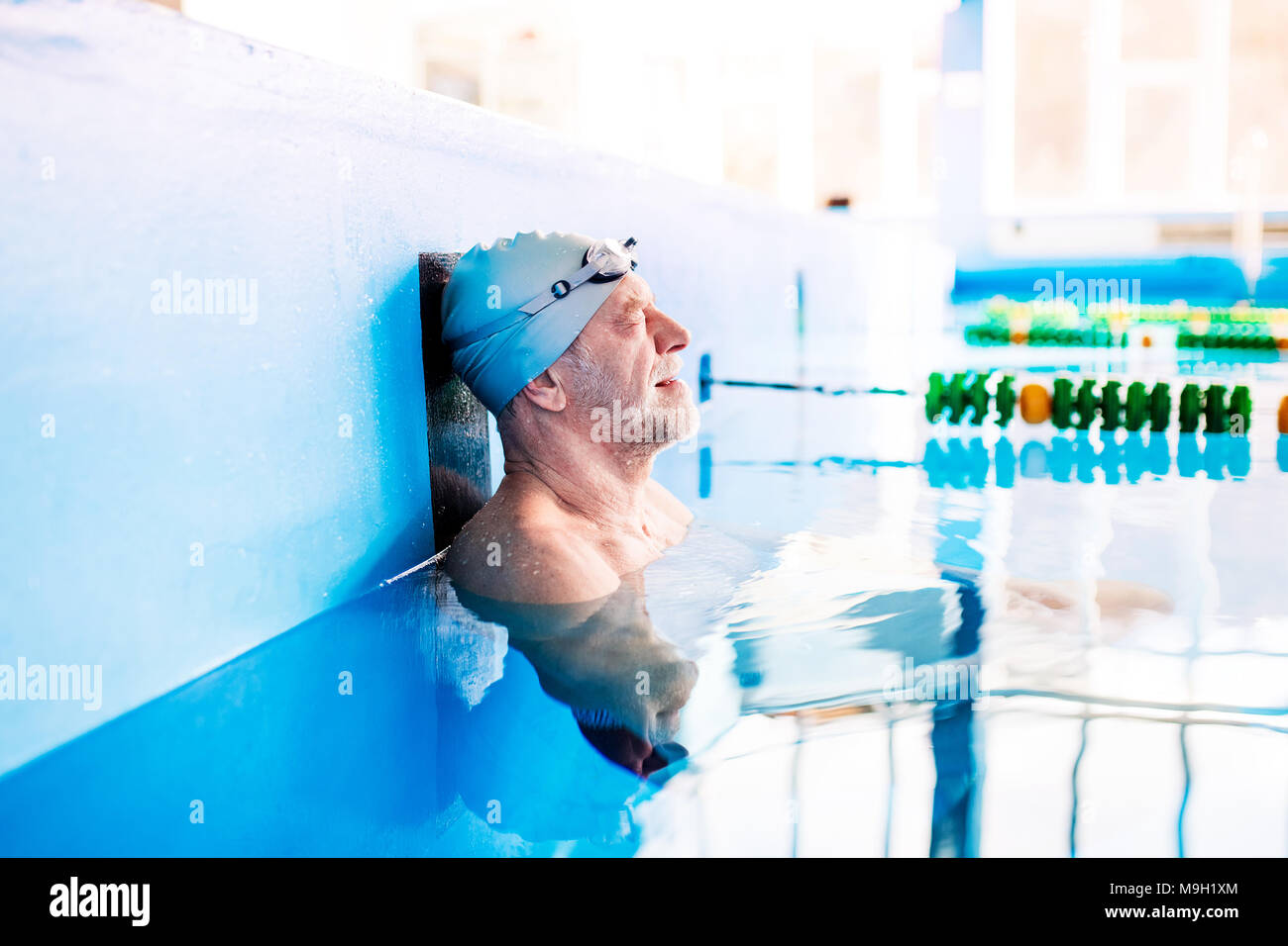 Senior nuoto uomo in piedi in acqua in una piscina coperta. Titolare di pensione o di rendita attiva godendo di sport. Foto Stock