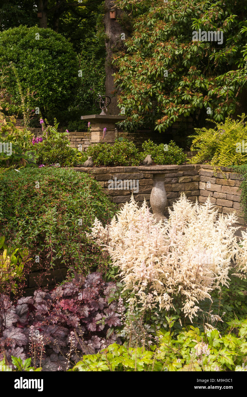 Piccola area terrazzata con pietra meridiana, bird bagno, a bordi rialzati, arbusti e piante - bella e tradizionale, giardino paesaggistico - Yorkshire, Inghilterra. Foto Stock