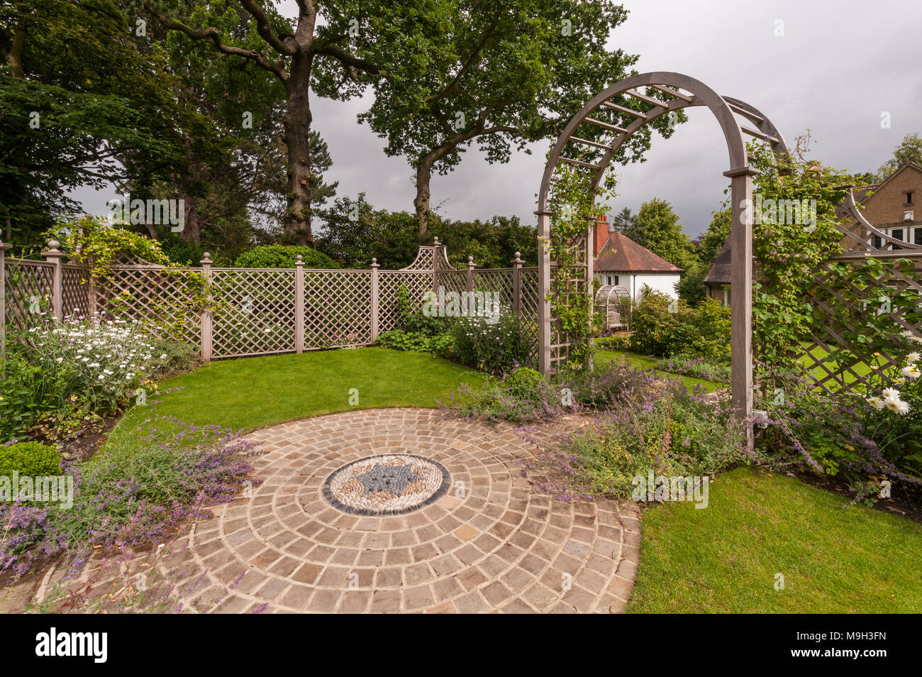 Piante, opere d'arte del mosaico, schermata trellis & arbour archway in estate - bella e tradizionale e paesaggistici, progettato giardino - West Yorkshire, Inghilterra, Regno Unito. Foto Stock