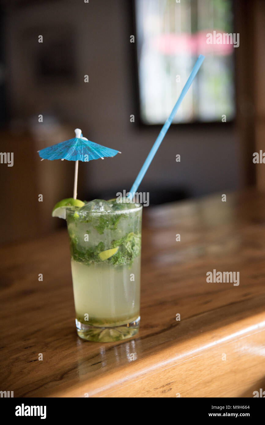 Un mojito bevanda alcolica si siede da solo su una barra. Un ombrello blu e paglia di riposo in vetro. Foto Stock