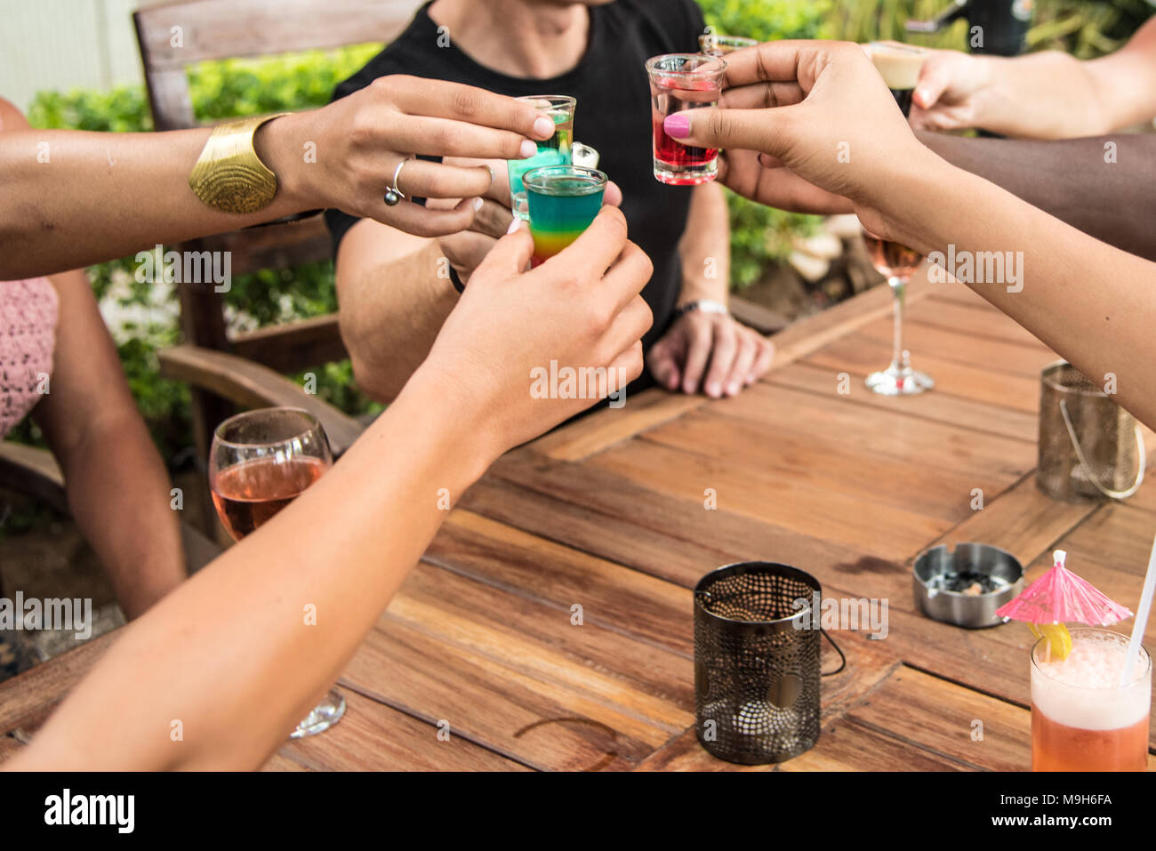 Un gruppo di braccia e mani colorate bicchierini di alcool si riuniscono durante un brindisi. Una varietà di toni della pelle può essere visto. Foto Stock