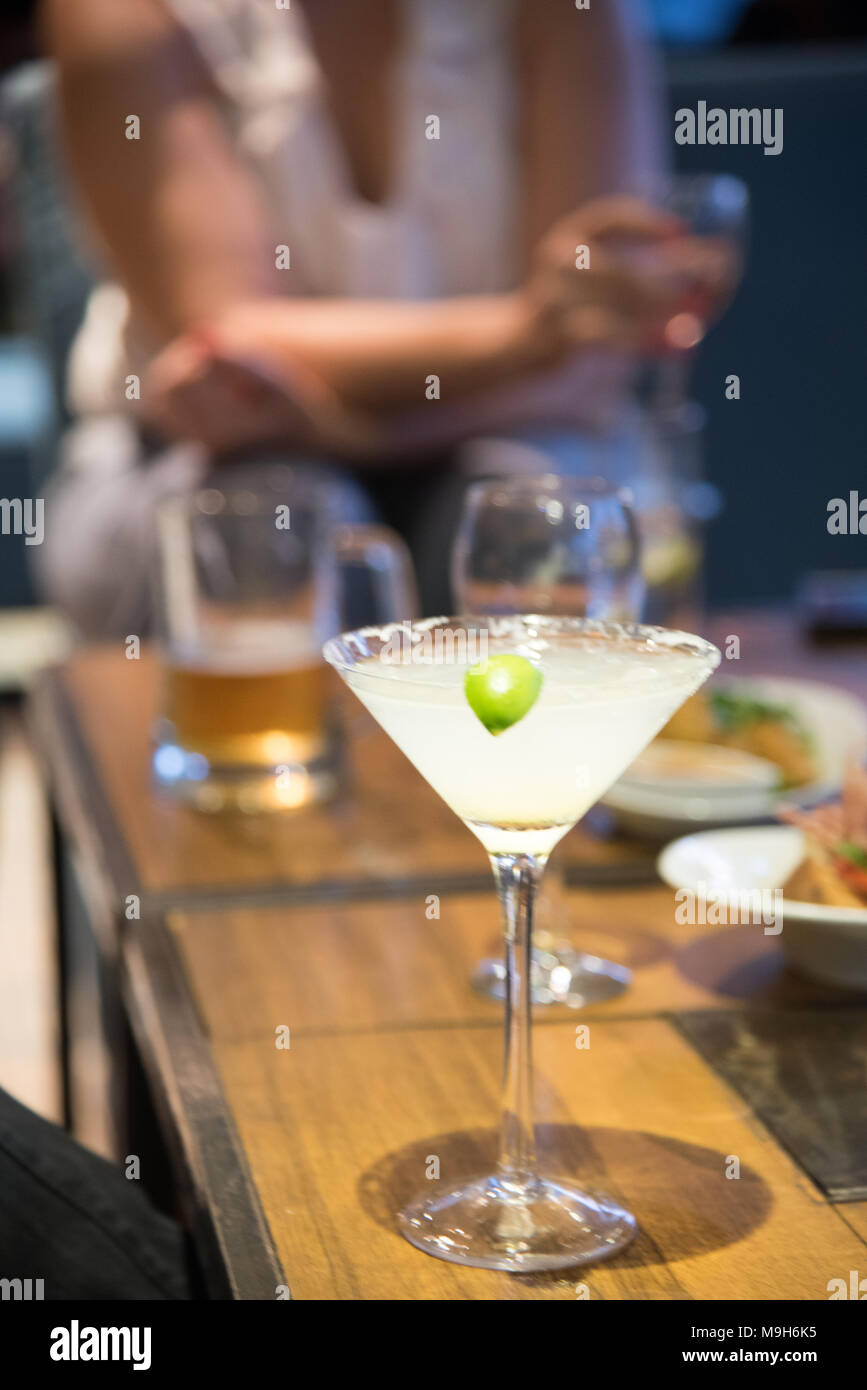 Un drink di margarita si siede su un tavolo nel fuoco. Sullo sfondo sono una varietà di bevande alcoliche, compresa la birra e il vino. Foto Stock