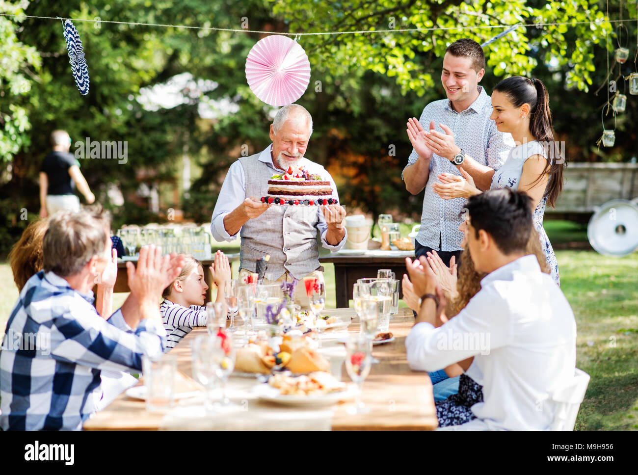 Festa di famiglia al di fuori nel cortile. Grande party in giardino. Festa di compleanno. Un anziano uomo con una torta di compleanno. Foto Stock