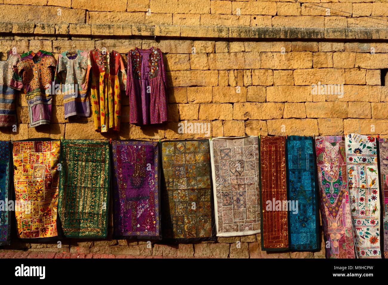 Variopinti tessuti indiani e vestiti appesi al giallo pareti di pietra arenaria di Jaisalmer Fort Rajashan India Foto Stock