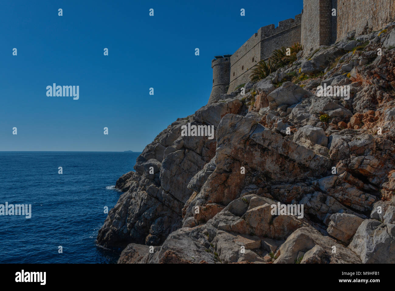 Una vista della cinta delle mura medievali della città di Dubrovnik, con rocce in primo piano che guarda al mare. Foto Stock