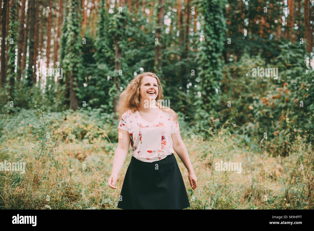 Giovani piuttosto Plus Size Caucasian sorridenti ragazza ridere donna con ondulato lungo marrone capelli In T-shirt bianco, Valzer Round In estate foresta verde. Foto Stock