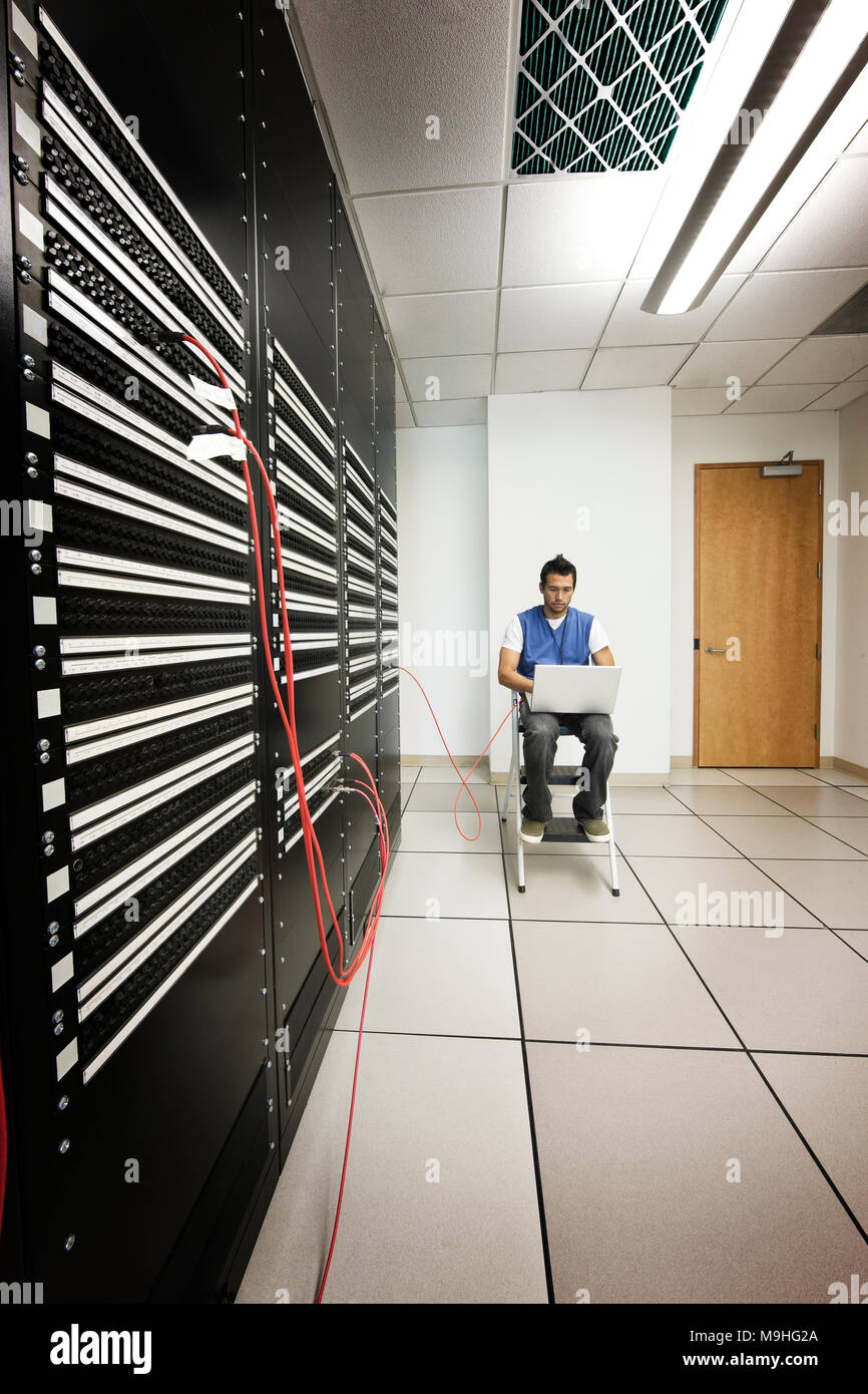 Computer tecnico che lavora su un computer portatile mentre si fa il lavoro diagnostico su un server in un computer più grande sala server. Foto Stock