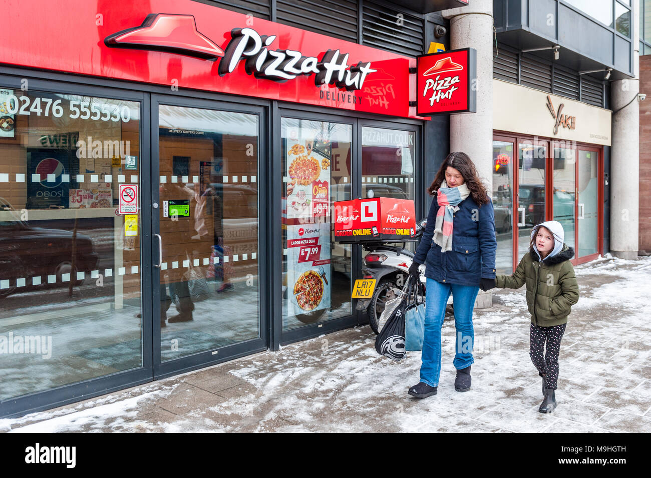Madre e figlia a piedi passato Pizza Hut a Coventry, West Midlands, Regno Unito con la neve sulla terra. Foto Stock