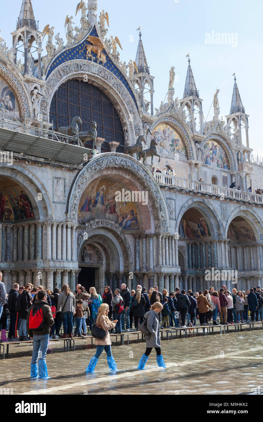 Acqua alta con le persone su un passarelle e guadare attraverso acqua davanti alla Basilica di San Marco, Piazza San Marco, Venezia, Veneto, Italia con sun flar Foto Stock