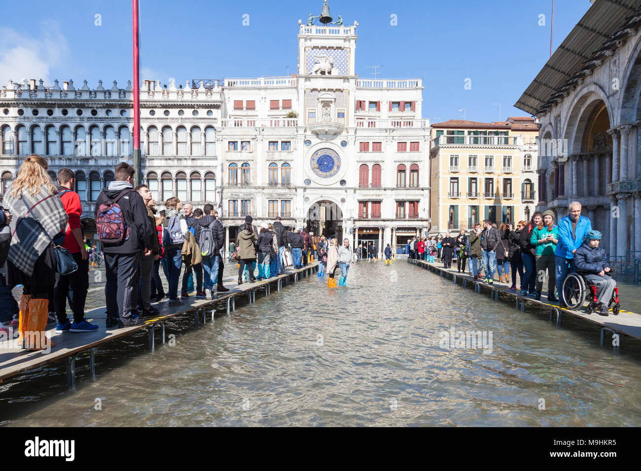 La gente che camminava sul passarelles in Piazza San Marco (Piazza San Marco) durante l'Acqua Alta inondazioni tra cui un ragazzo su una sedia a rotelle, Venezia, Veneto, Foto Stock