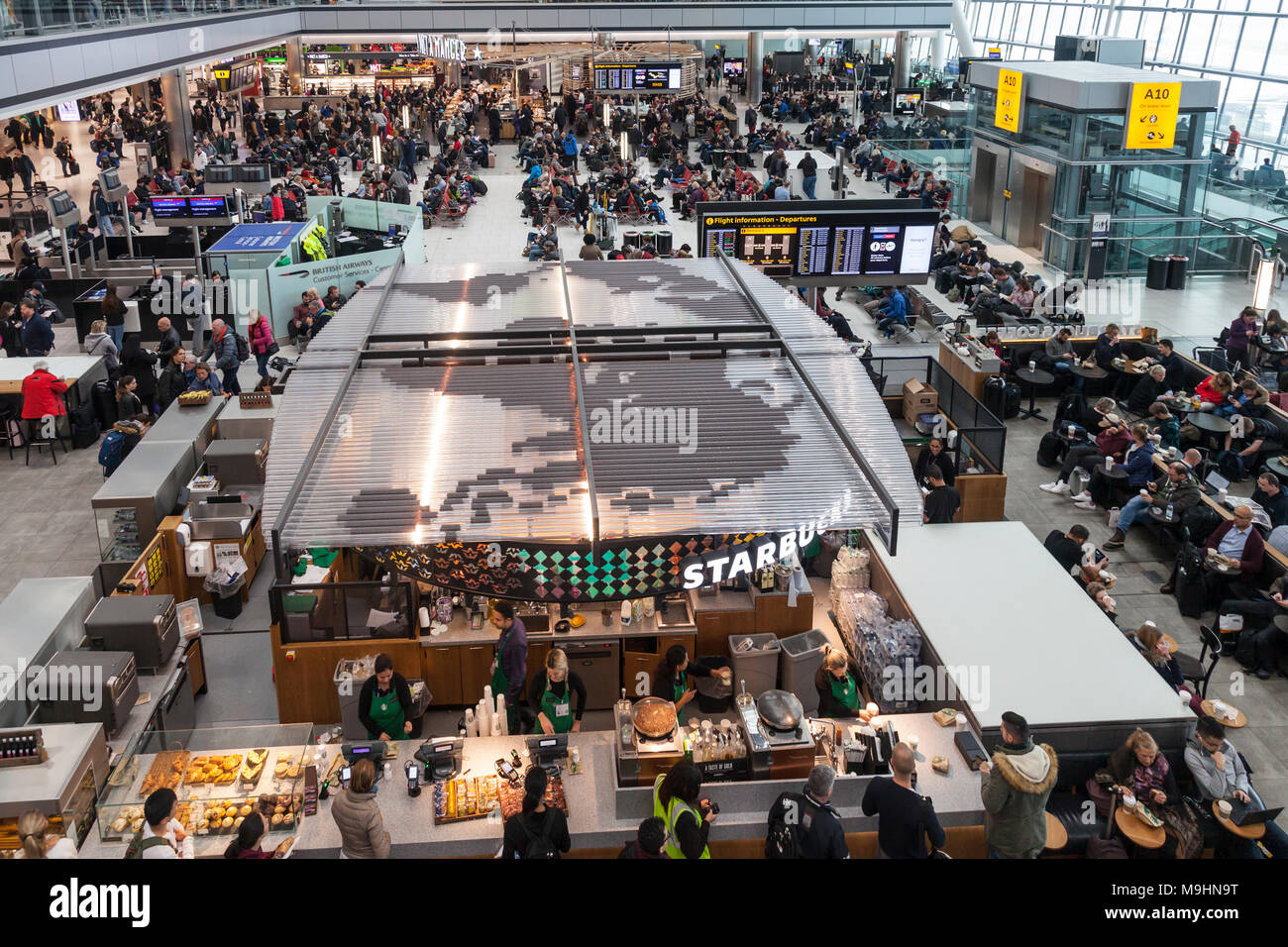 Aeroporto di Heathrow Terminal 5 sala partenze e concourse. Grande mappa del mondo sul tetto di Starbucks in uscita. Occupato con i passeggeri in un giorno di molti fli Foto Stock