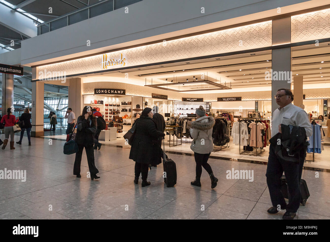 Uscire aria passeggeri in viaggio al di fuori dei magazzini Harrods retail outlet in aeroporto di Heathrow, terminale 5, Londra, Inghilterra, Regno Unito. Foto Stock
