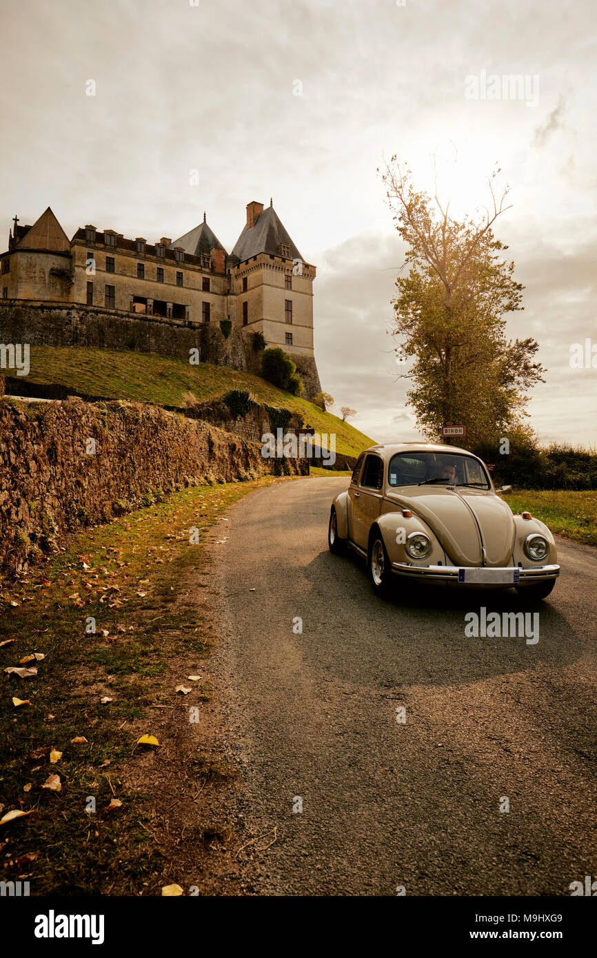 Un classico VW Beetle rigidi passato il Château de Biron un castello nella valle del Lède nel comune di Biron in Dordogne Francia. Foto Stock