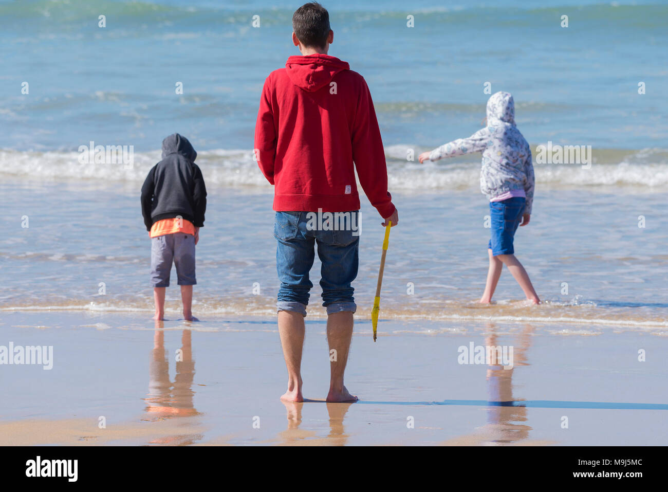 Un padre guardando i suoi figli giocare in mare a Fistral Beach in Newquay Cornwall. Foto Stock
