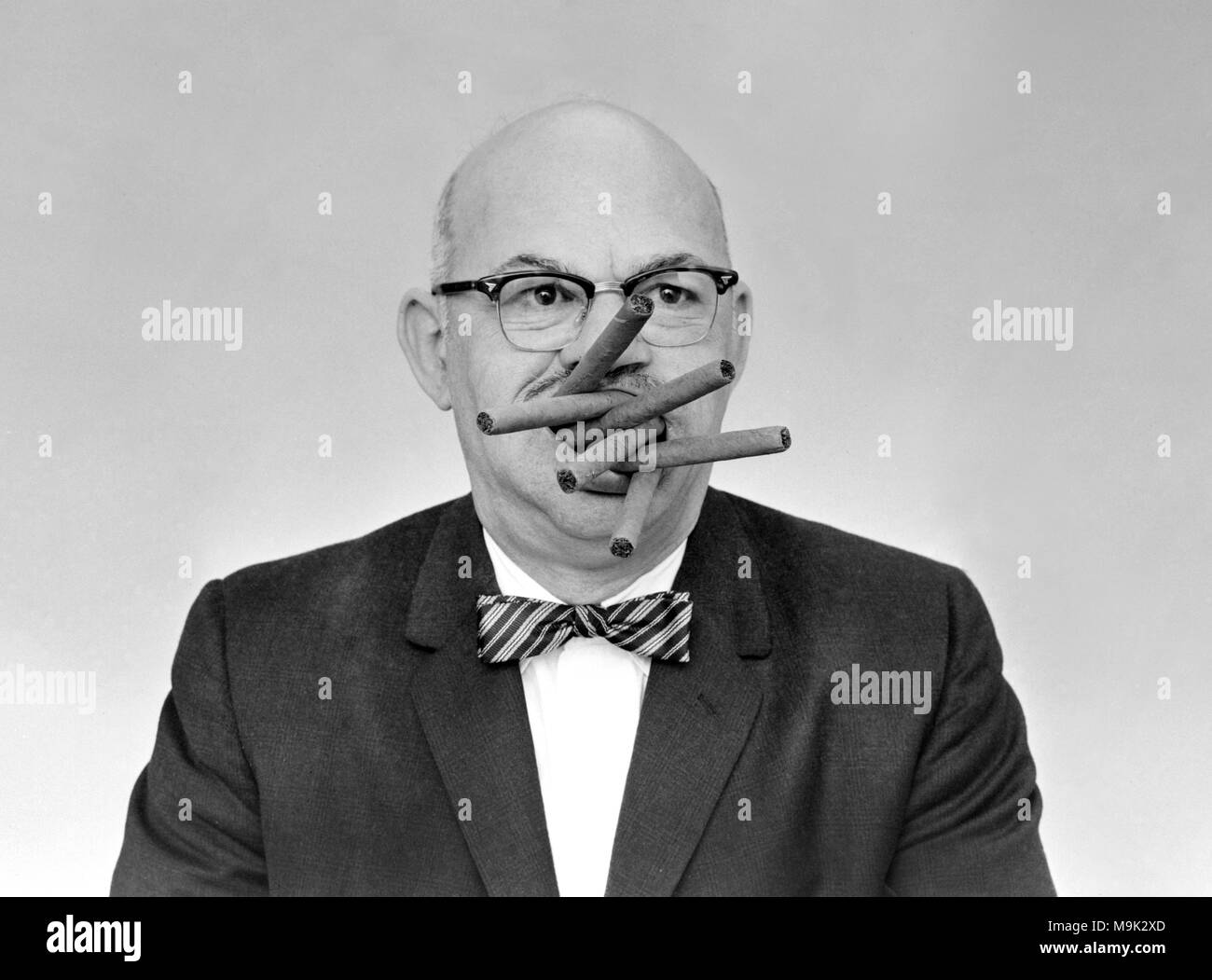 Un uomo sente il bisogno di cram sei sigari in bocca in una volta, ca. 1962. Foto Stock