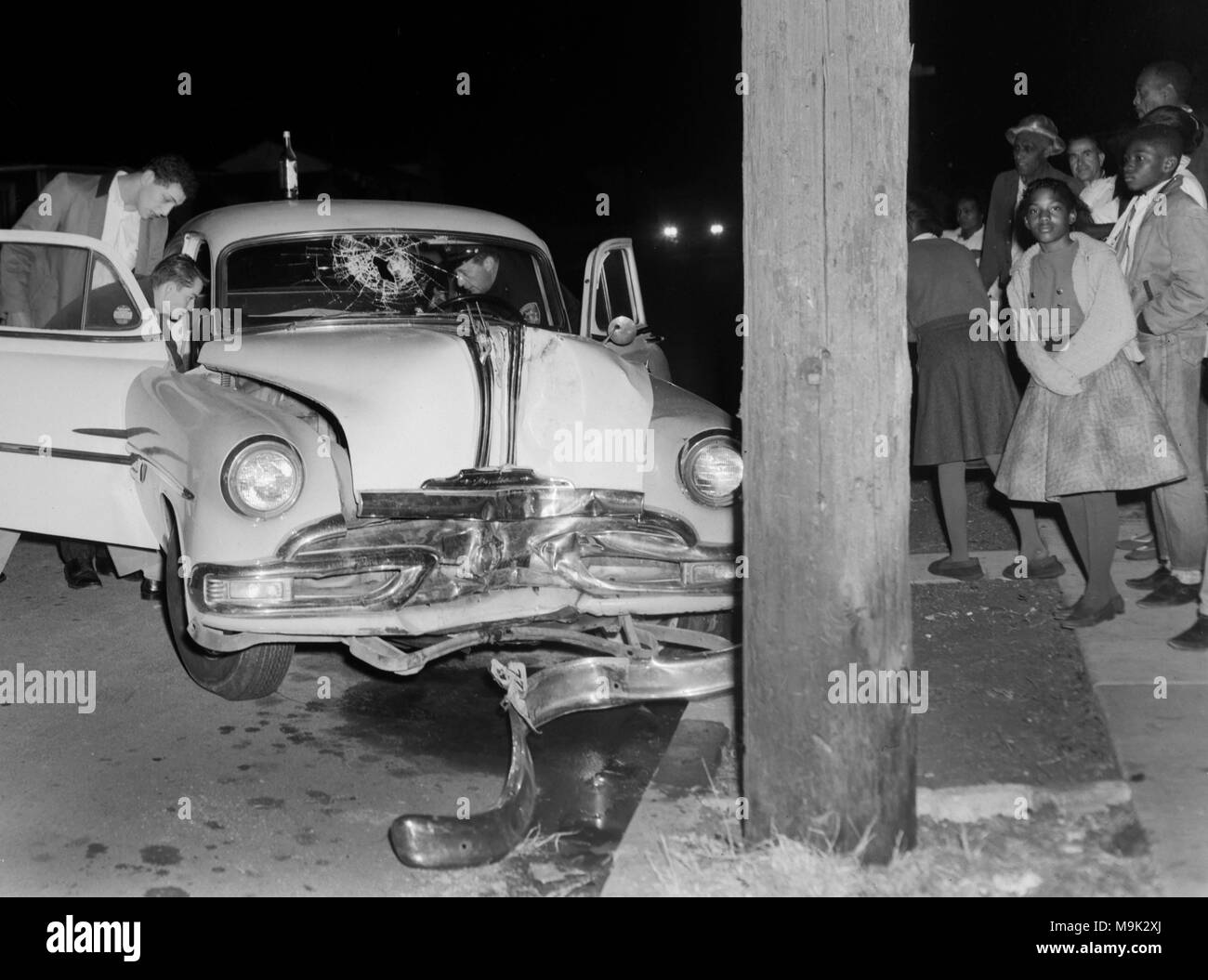 Con curiosi guardando, lavoratori di emergenza estrarre un driver da un crash car a Oakland, in California, ca. 1961. Una bottiglia di birra si trova appollaiato sul tetto dell'auto. Foto Stock