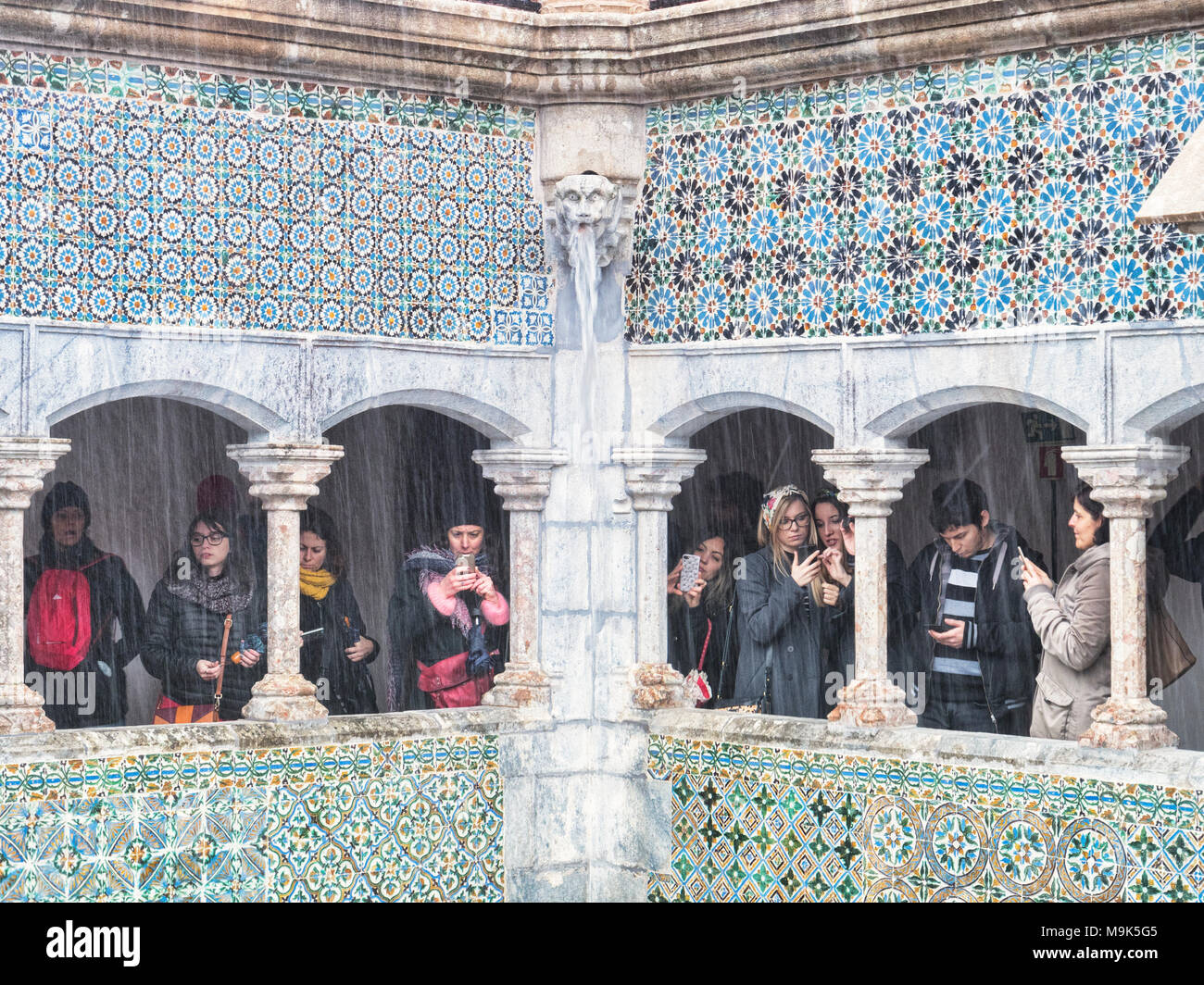 5 Marzo 2018: Sintra, Portogallo - i turisti con i telefoni con fotocamera sotto un porticato al Pena Palace, rendendo più molto di un giorno di pioggia. Foto Stock