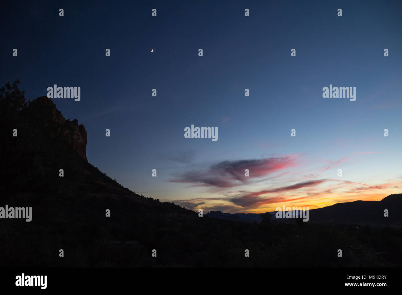 Deep maroon, viola e arancione tingono il cloud vicino orizzonte fornisce colorato contrappunto alla sagoma scura di red rock bluff in Sedona mentre la luna sorge Foto Stock