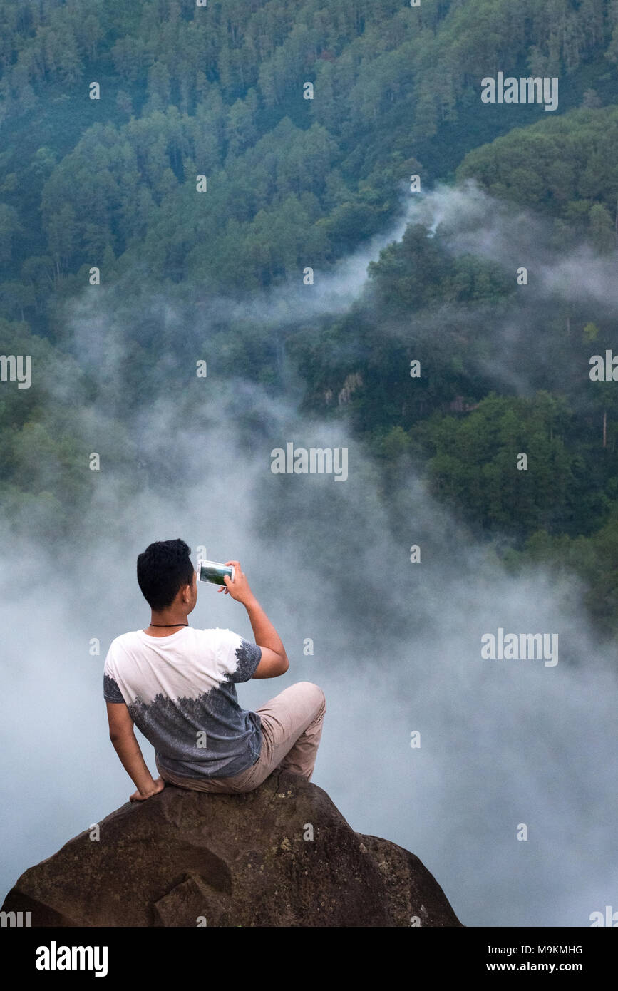 Un giovane uomo di scattare una foto di brumoso paesaggio con lo smartphone in Lembang, West Java, Indonesia. Foto Stock