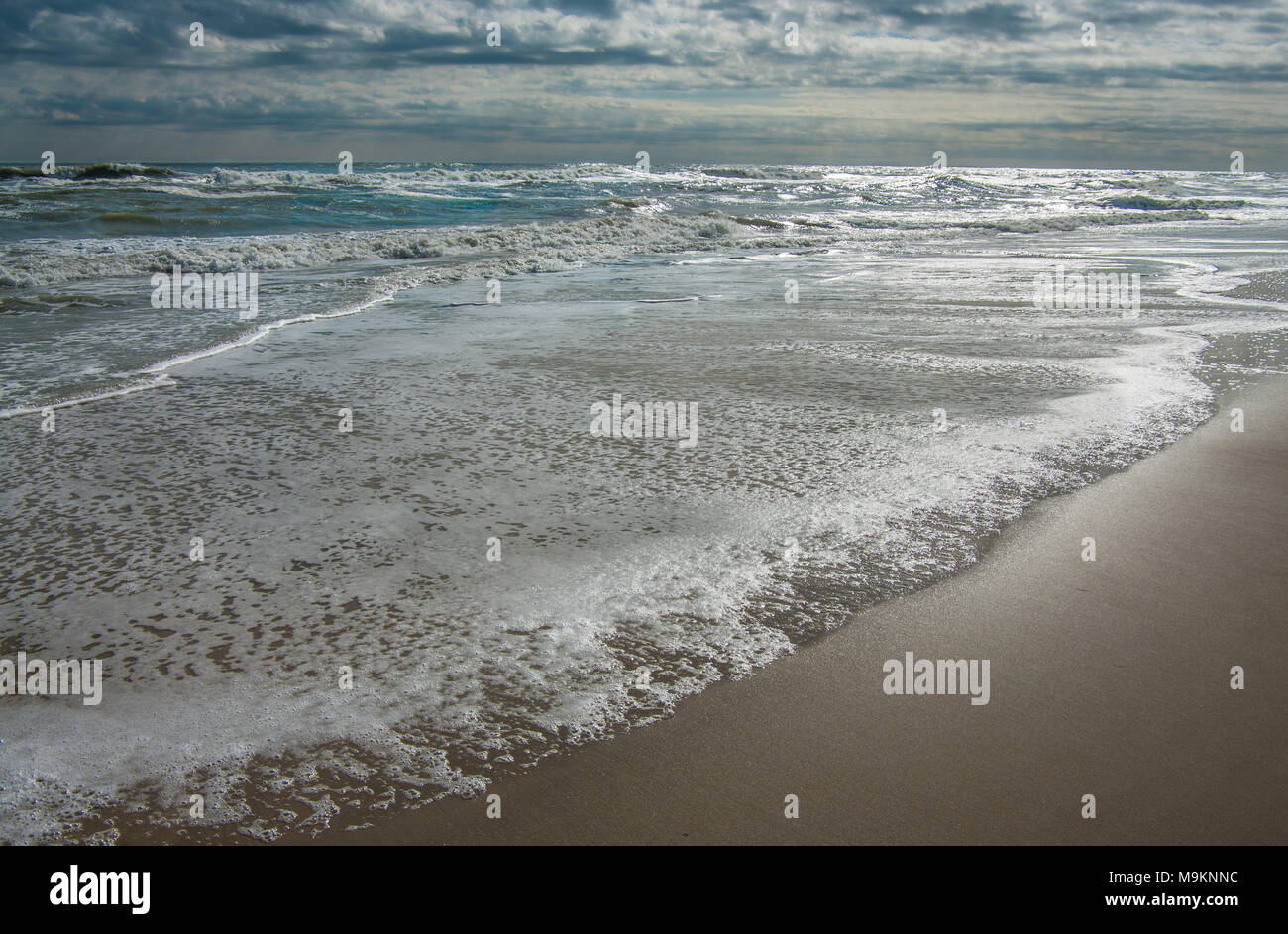 Modifica di marea: onde in arrivo coprire la spiaggia come un cielo scuro inizia a schiarirsi a Cape Hatteras National Seashore. Foto Stock