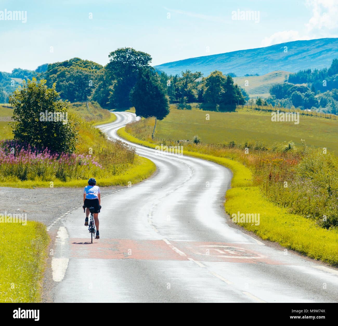 Ciclista femmina sulla A689 al di fuori di Milton vicino a Brampton, Cumbria con vista verso il North Pennines Foto Stock