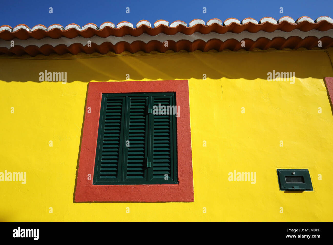 Finestra rossa sulla parete gialla con persiane verdi e motivi di tetto in terracotta Foto Stock