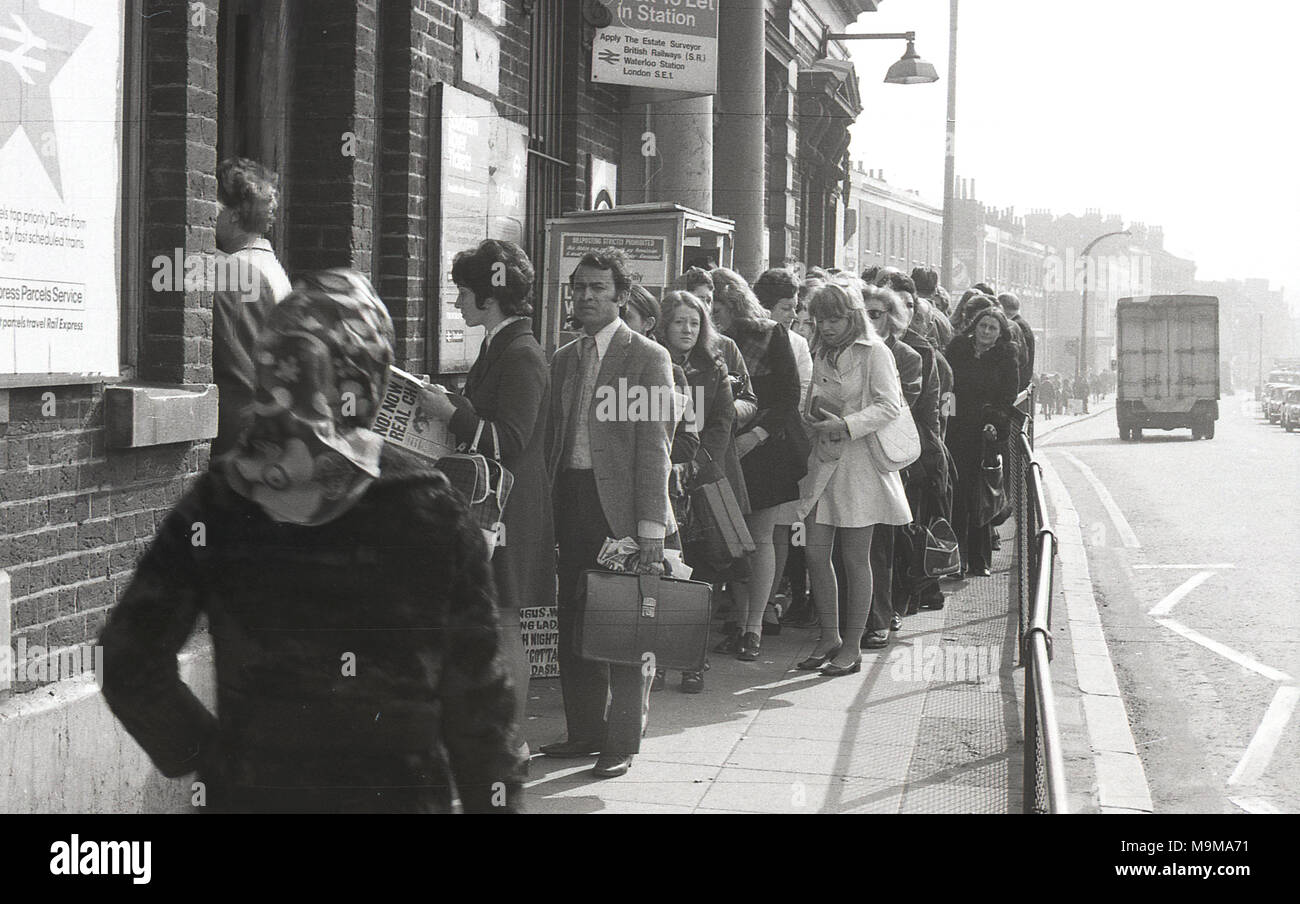 Anni Settanta, storico, passeggeri ferroviari in coda sul marciapiede fuori New Cross stazione ferroviaria nel sud est di Londra, Inghilterra. In questo momento, scioperi e annullato treni erano un evento comune su British Rail e in questo caso le piattaforme sono state troppo piena di prendere più passeggeri. Foto Stock