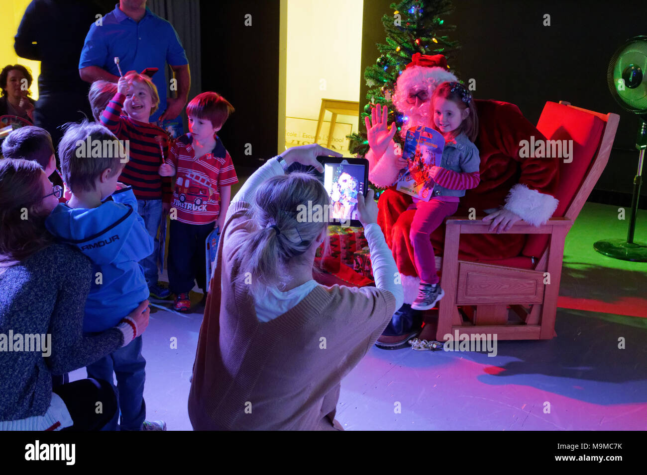 Una madre utilizzando un ipad per fotografare un bambino seduto con Babbo Natale Foto Stock