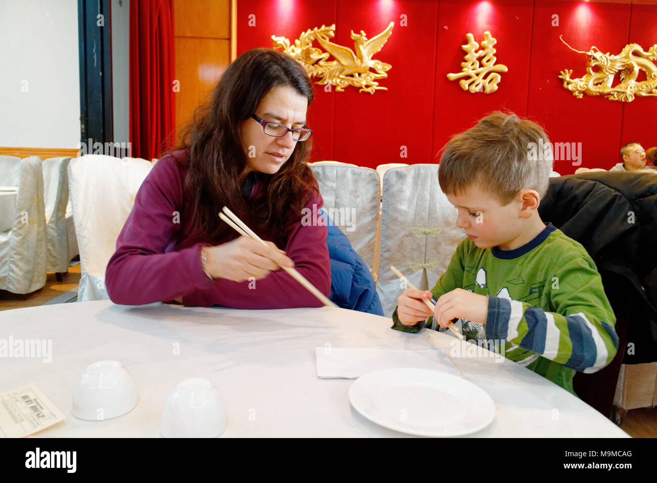 Una Madre che mostra il suo bambino di 5 anni come utilizzare bacchette in un ristorante cinese Foto Stock