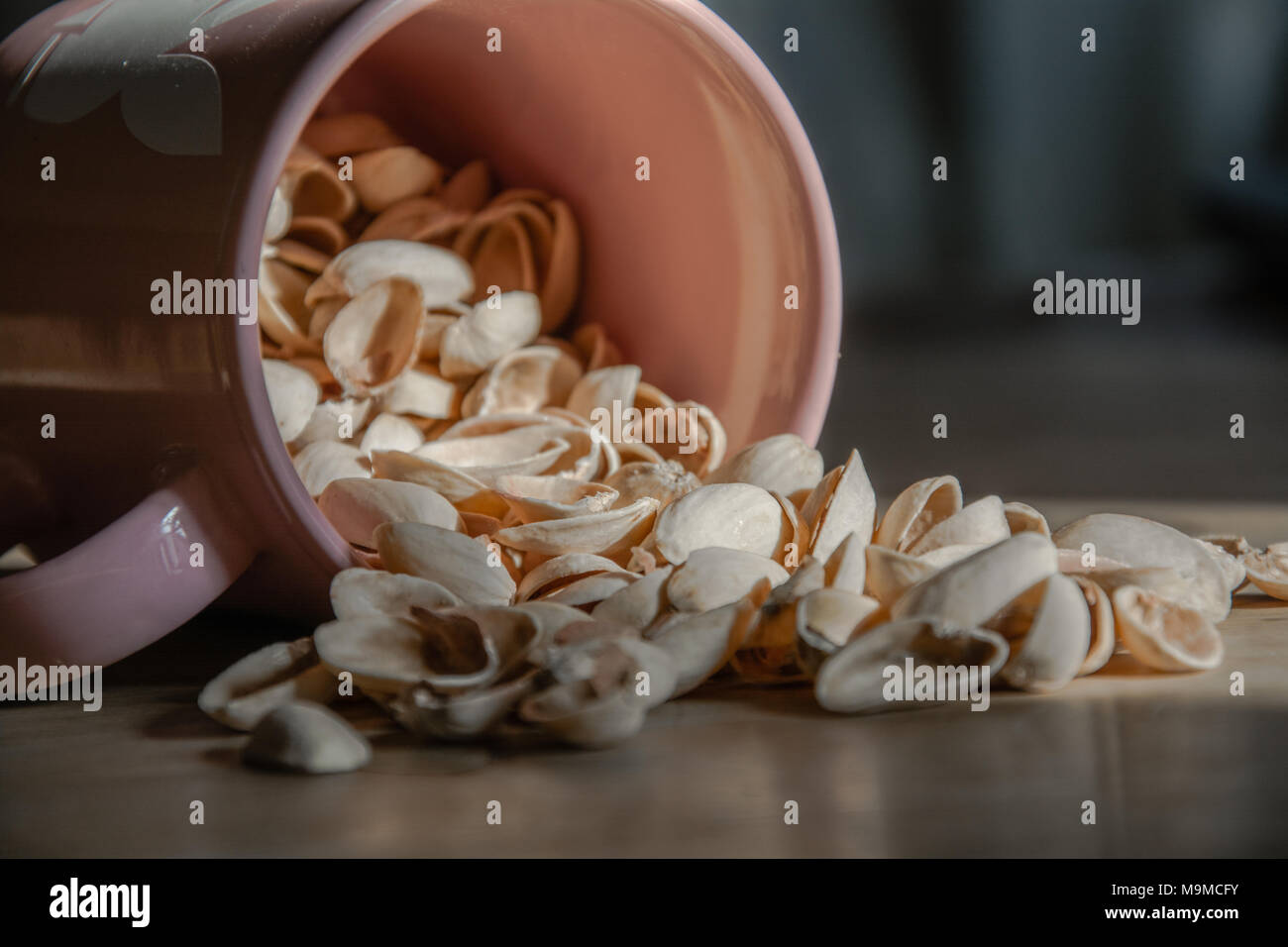 Pistacchio gusci fuoriuscita di una tazza rosa su di una superficie di legno. Potrebbe riferirsi a snack salati. O potrebbe essere il concetto di 'dadi' Foto Stock
