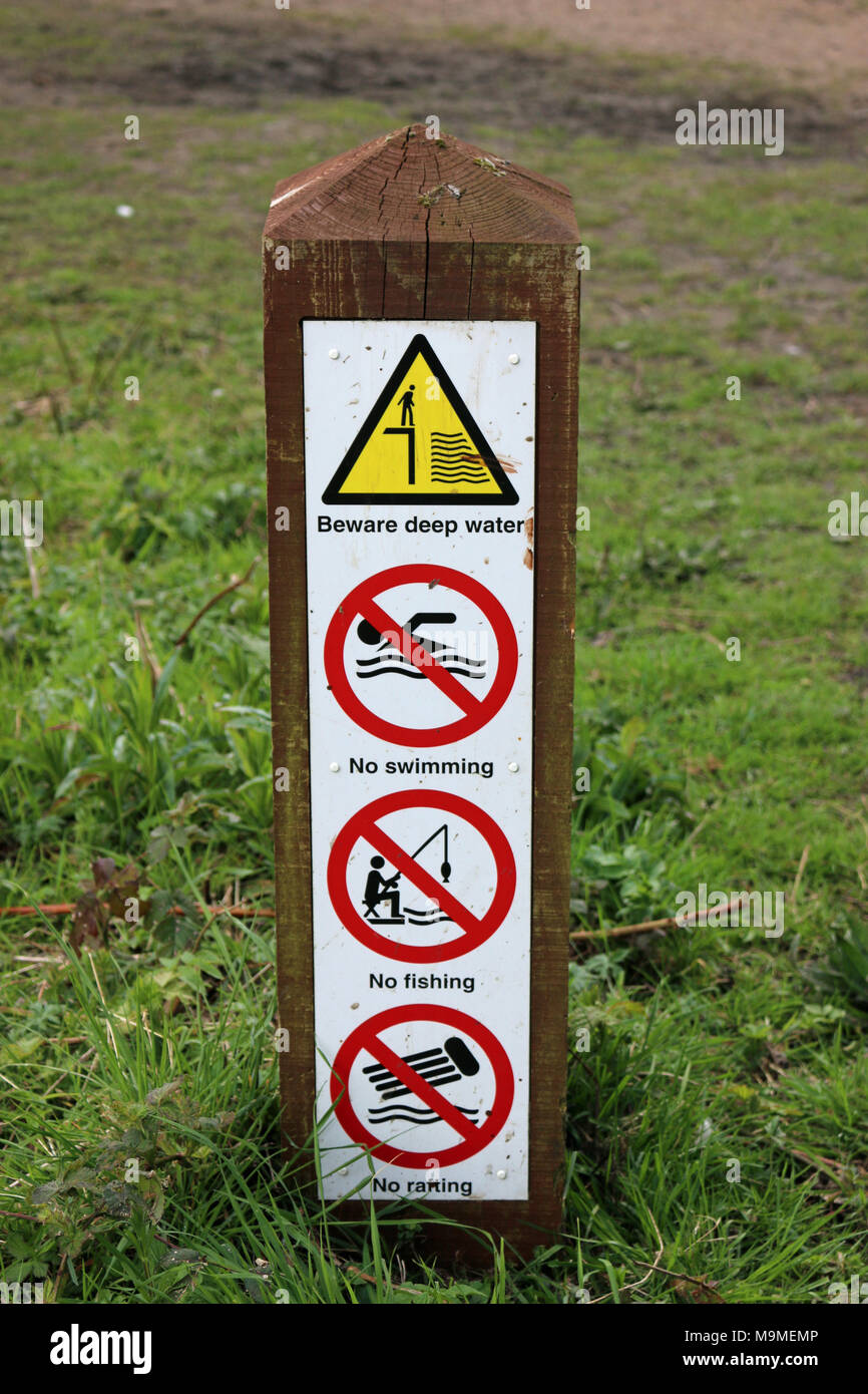 Pond cartelli di avvertimento in un parco su un palo di legno consigliando di acqua profonda, no il nuoto, la pesca e il rafting non con uno sfondo di erba. Foto Stock