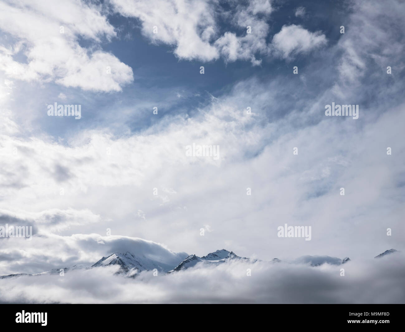 Cielo nuvoloso con neve coperto vette emergenti dalla nebbia. Foto Stock