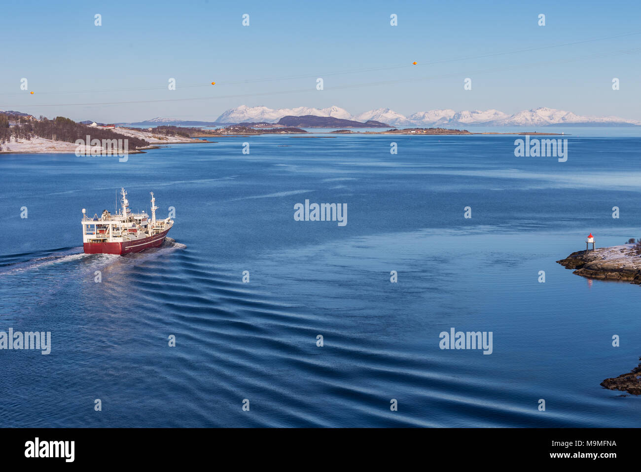 Una barca passa un faro in Tjeldsundet strait, separando la terraferma della Norvegia dall isola di Hinnoya Foto Stock