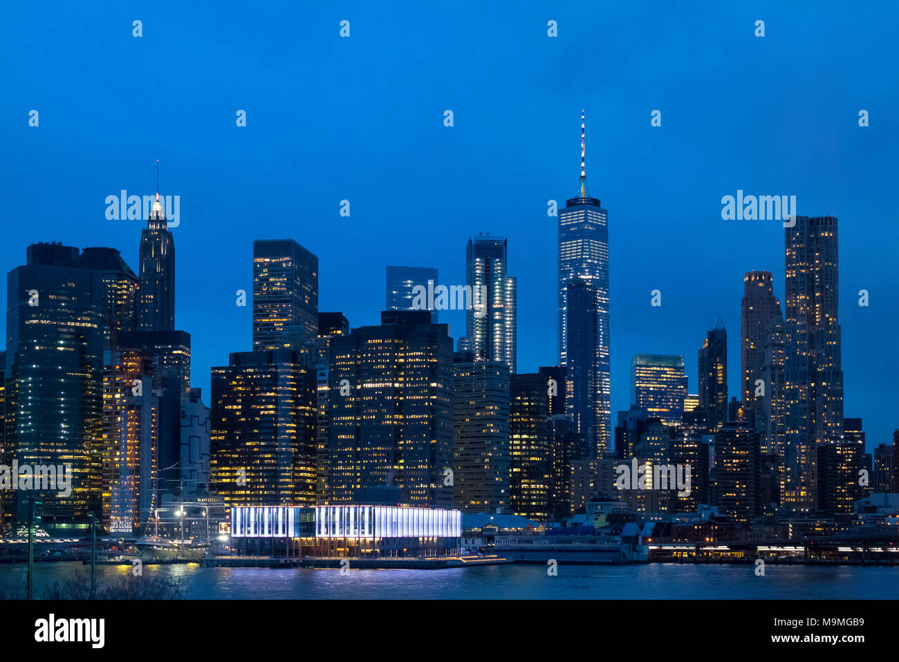 La parte inferiore di Manhattan skyline che si vede attraverso l'East River mostra le luci della città e le luci accese in Pier 17 Foto Stock